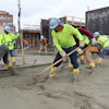 Construction workers in safety gear spreading concrete at urban building site