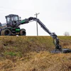 Green and black forestry harvester machine extending long mechanical arm across grassy field