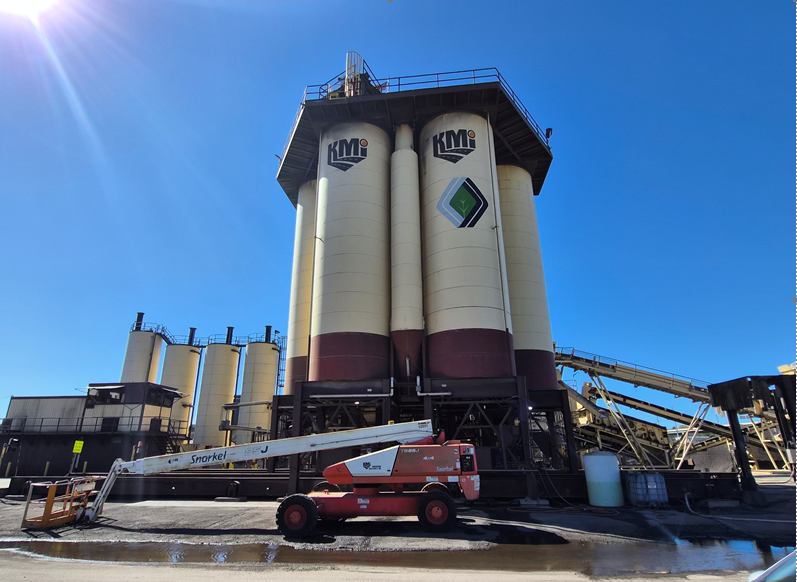 KMG industrial facility with large white and maroon storage silos and red telescopic crane