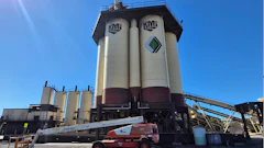 KMG industrial facility with large white and maroon storage silos and red telescopic crane