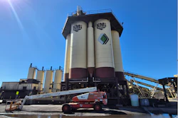 KMG industrial facility with large white and maroon storage silos and red telescopic crane