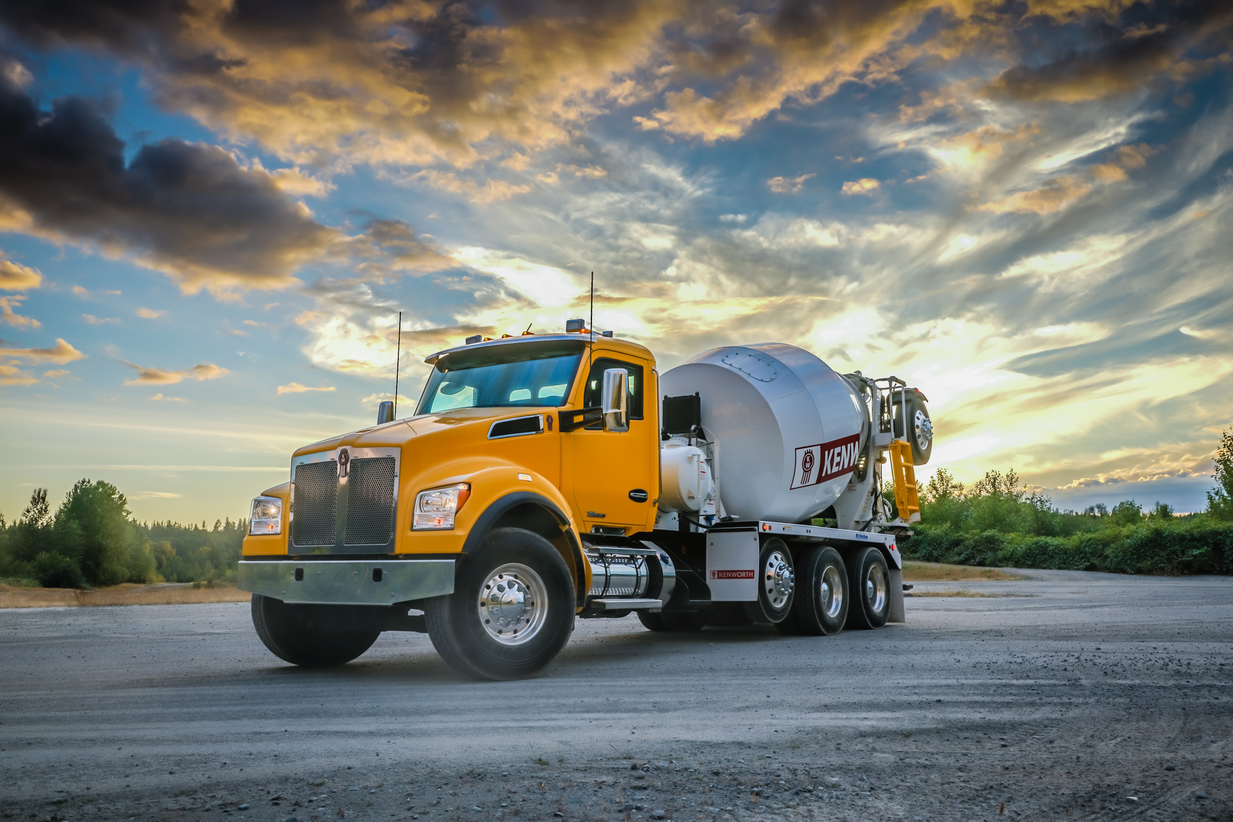 Yellow Kenworth concrete mixer truck parked on asphalt with dramatic sunset sky