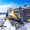 Yellow Volvo excavator on rocky snow-covered terrain with mountain backdrop