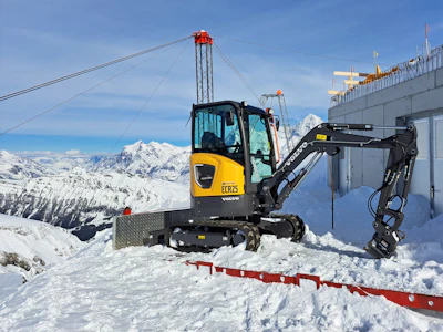 Yellow Volvo excavator on snowy mountain slope near ski lift infrastructure