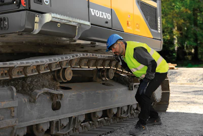 Construction worker inspecting Volvo excavator tracks on job site