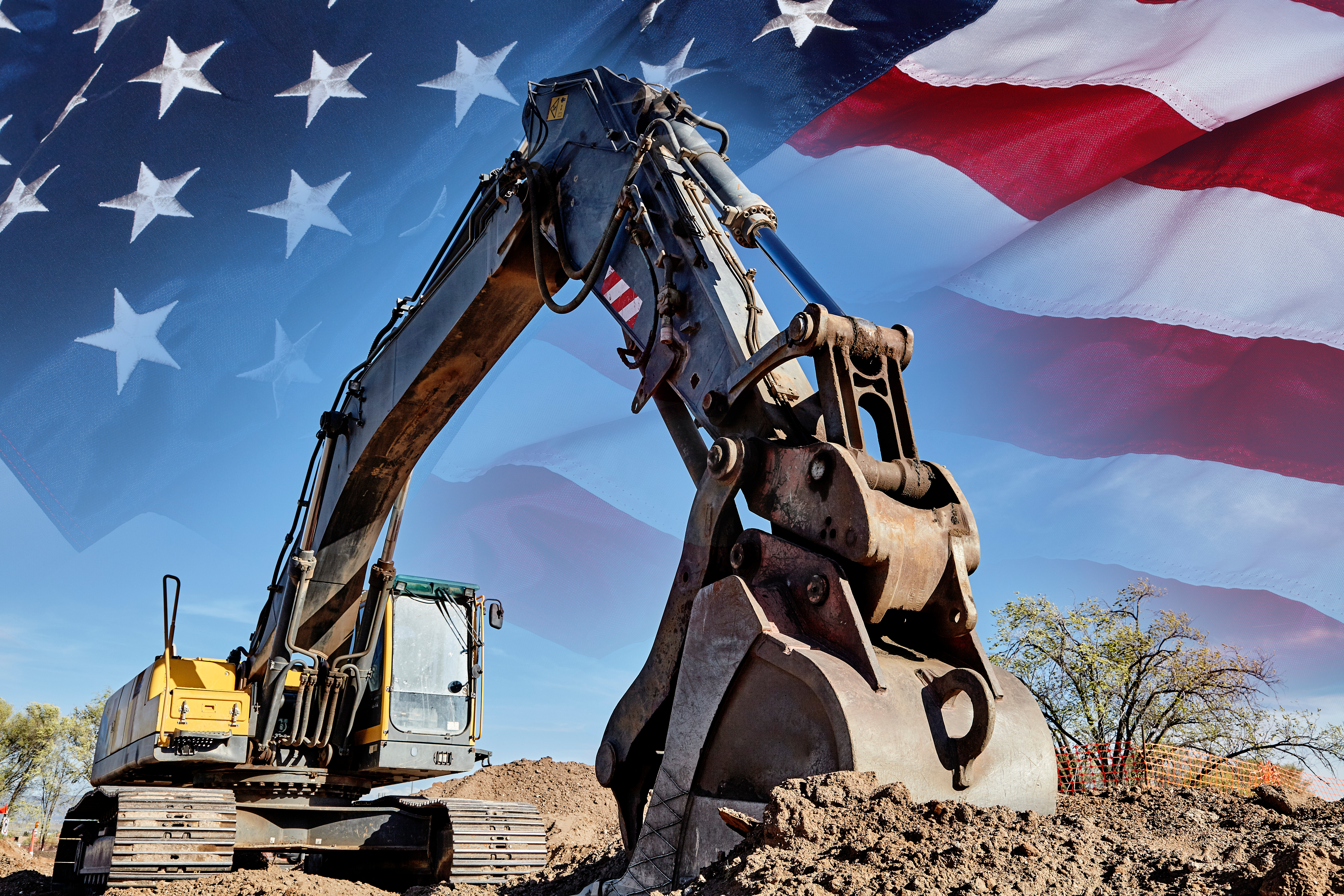 Yellow excavator digging dirt with American flag waving in background