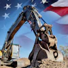 Yellow excavator digging dirt with American flag waving in background
