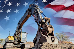 Yellow excavator digging dirt with American flag waving in background