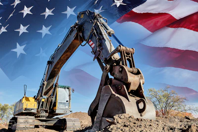 Yellow excavator digging dirt with American flag waving in background