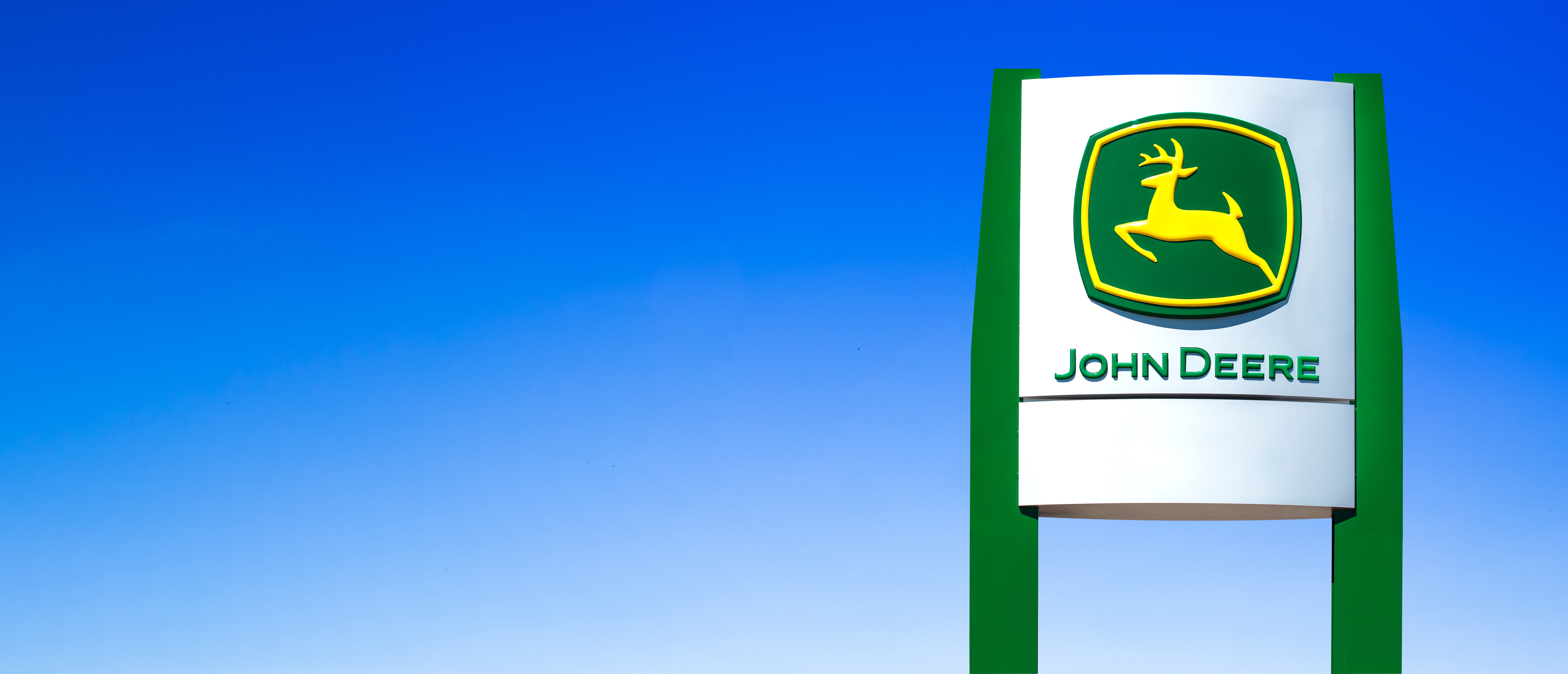 John Deere green and yellow logo sign against bright blue sky
