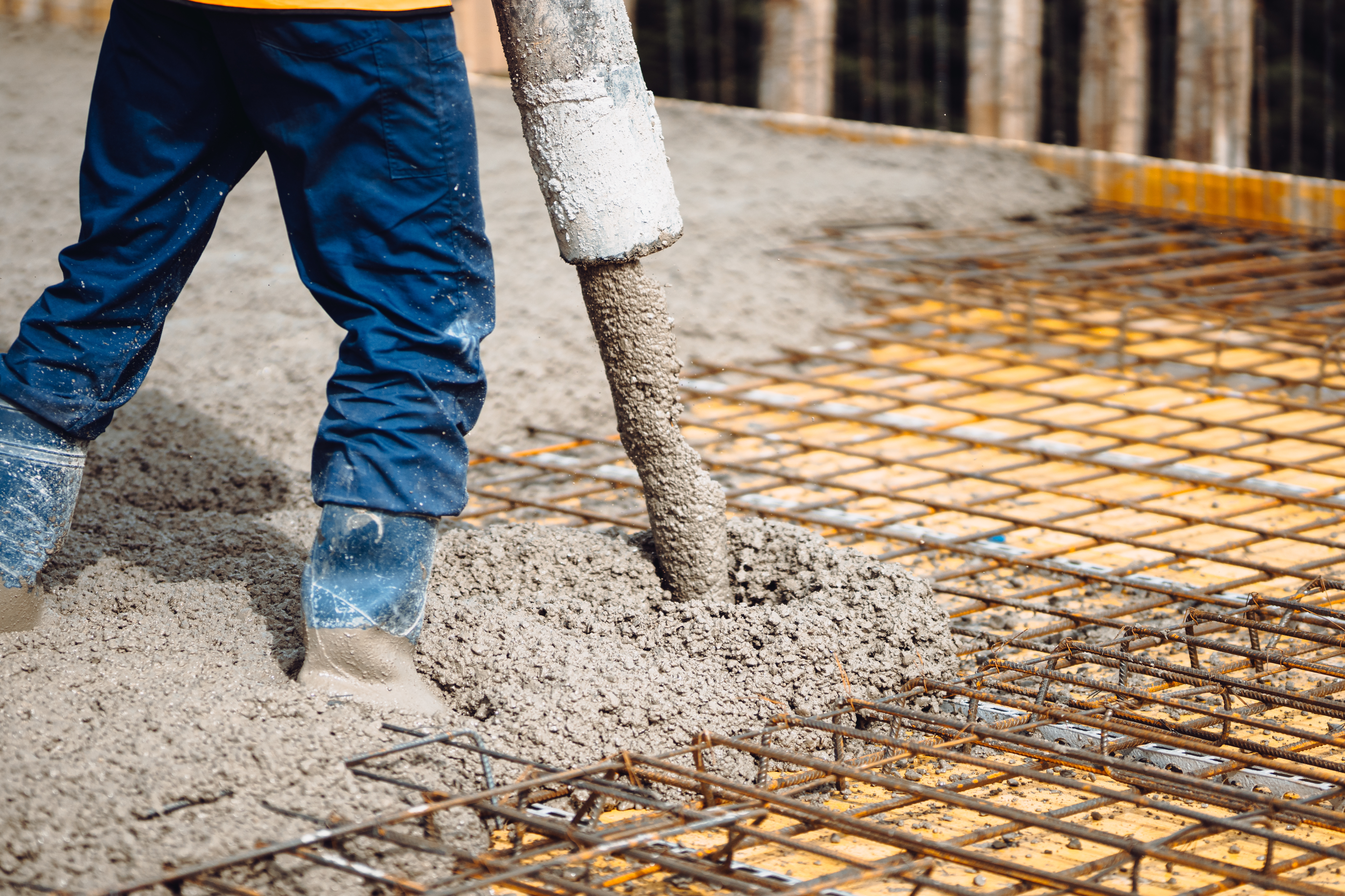 Construction worker pouring concrete over steel reinforcement mesh