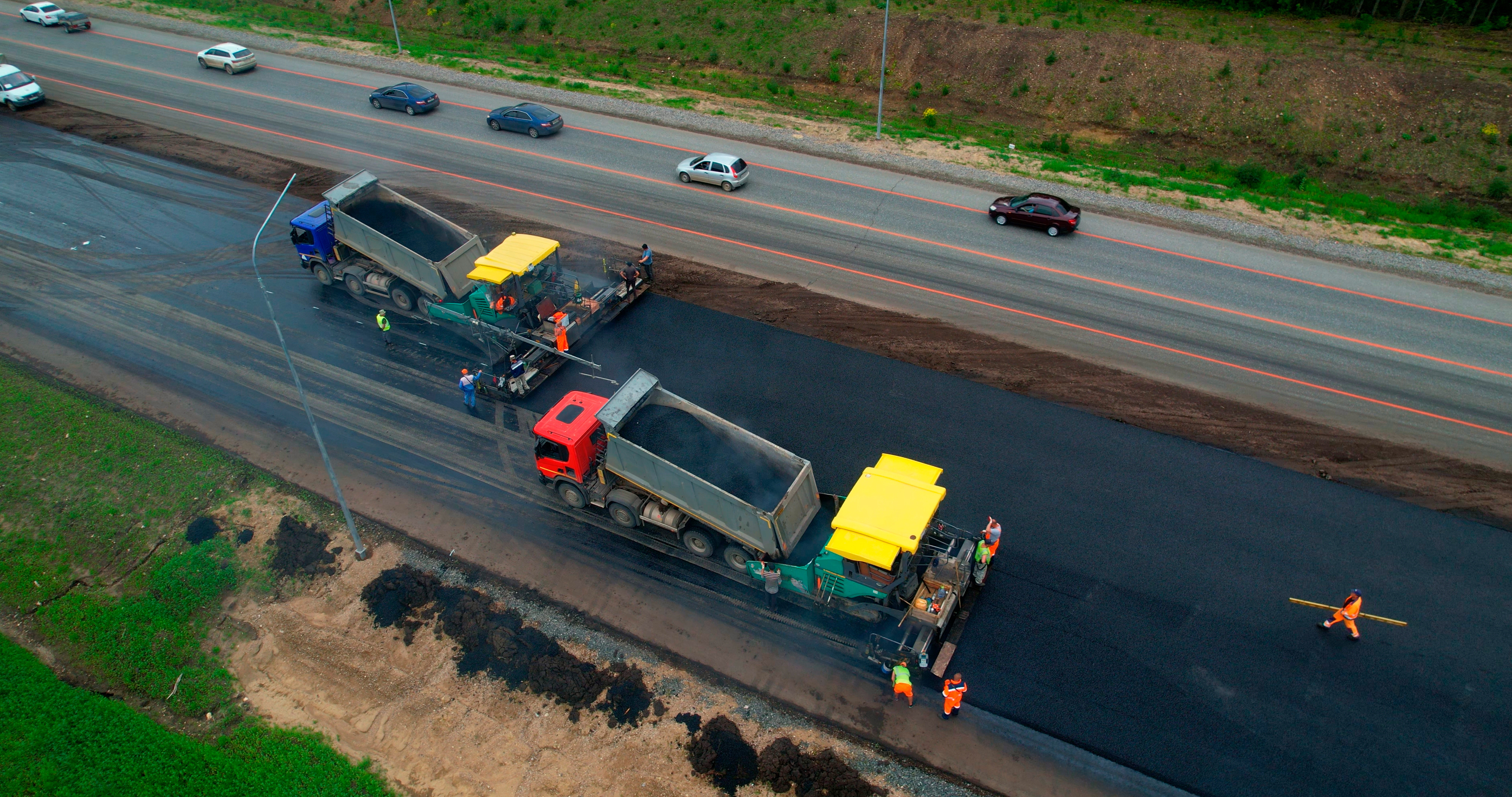 Road paving machinery resurfacing highway with dump trucks and construction workers