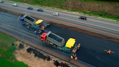 Road paving machinery resurfacing highway with dump trucks and construction workers