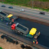 Road paving machinery resurfacing highway with dump trucks and construction workers