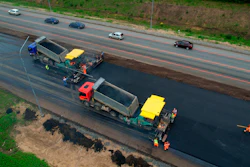 Road paving machinery resurfacing highway with dump trucks and construction workers