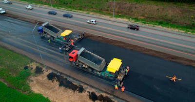 Road paving machinery resurfacing highway with dump trucks and construction workers