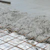 Wet concrete being poured over steel reinforcement grid during construction