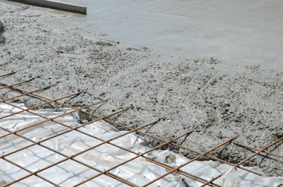 Wet concrete being poured over steel reinforcement grid during construction
