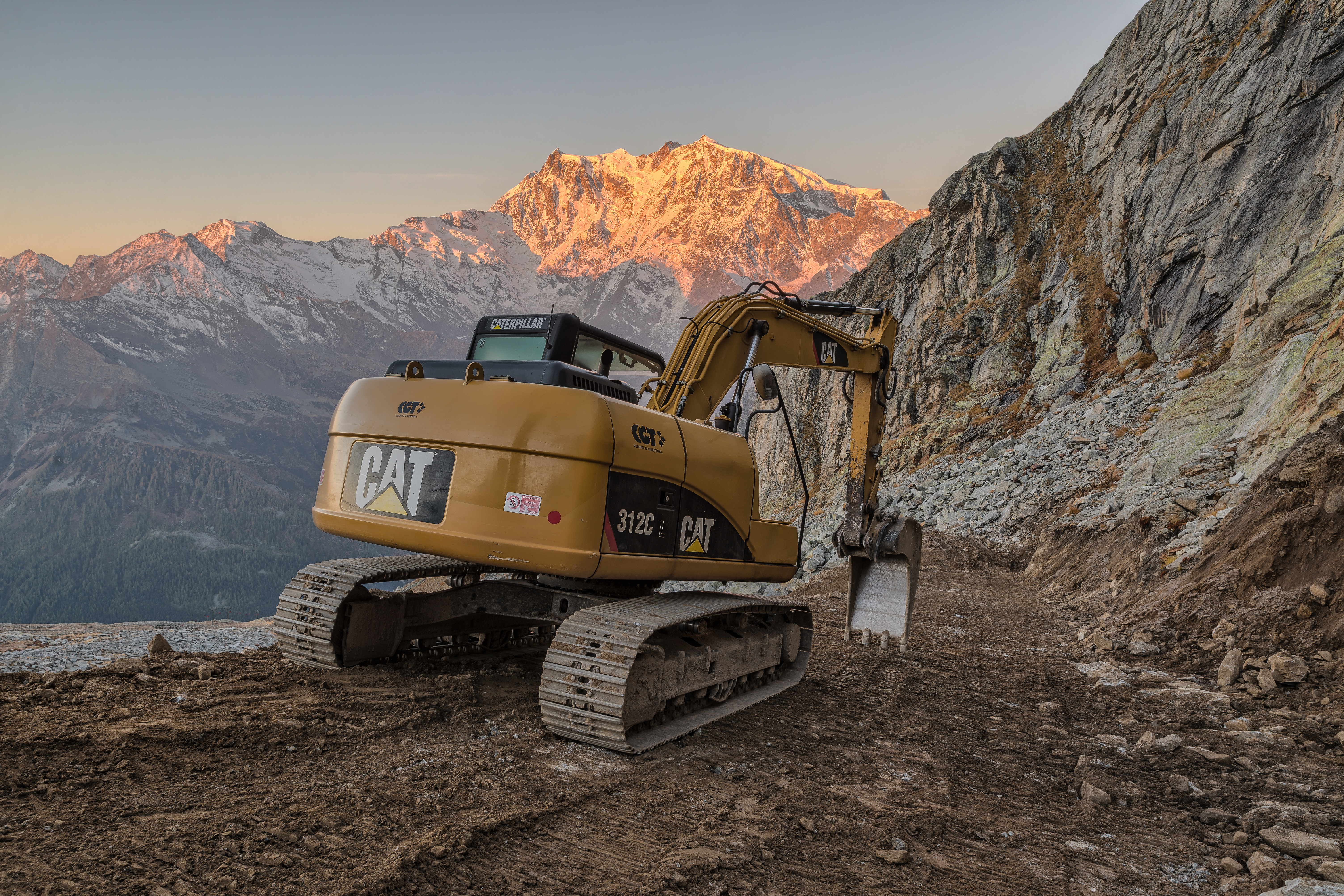 Yellow CAT excavator on rocky mountain path at golden sunrise