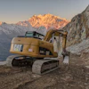 Yellow CAT excavator on rocky mountain path at golden sunrise