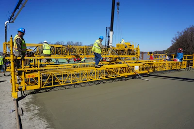 Construction workers operating yellow concrete paving machine on roadway project