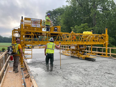 Yellow concrete paving machine on construction site with workers in safety vests
