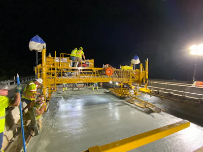 Night road construction crew operating concrete paving machine on highway