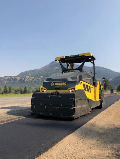 Yellow Bomag road paver laying asphalt on mountain highway construction site