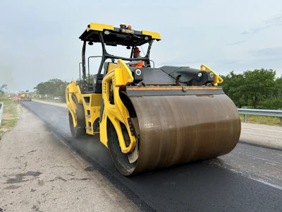 Yellow road roller compacting fresh asphalt on highway construction site