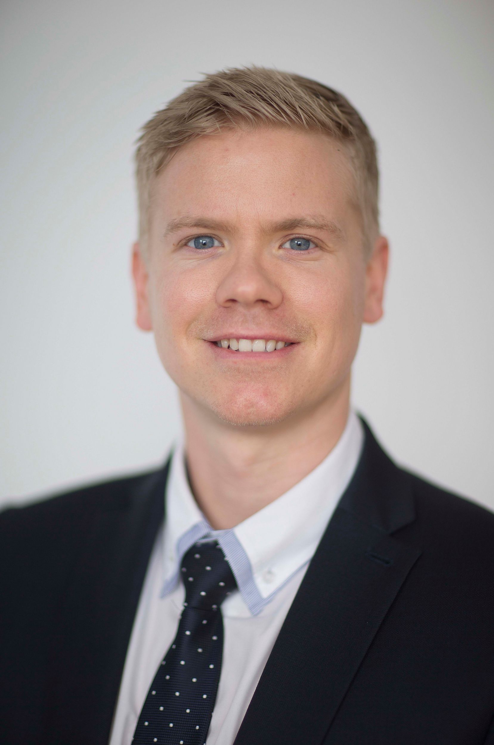 Professional smiling man in black suit and polka dot tie against neutral background