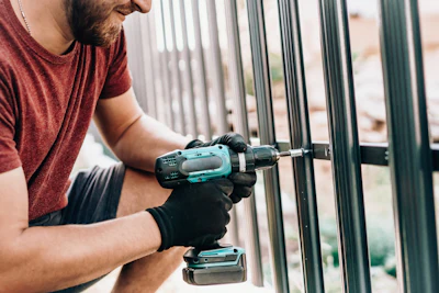 Worker drilling metal fence wearing black gloves and red shirt