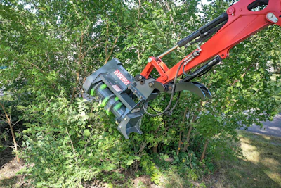 Red and gray mechanical excavator attachment clearing vegetation among green trees