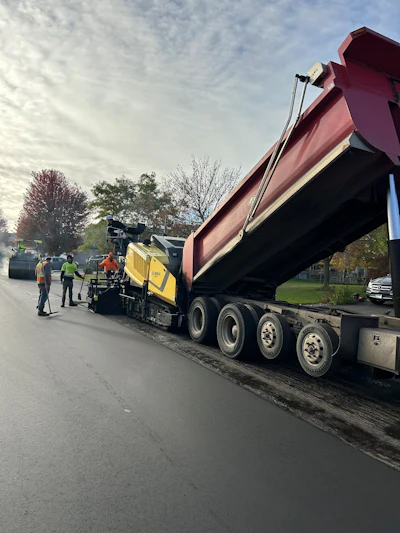 Road paving equipment with dump truck and asphalt spreader on suburban street