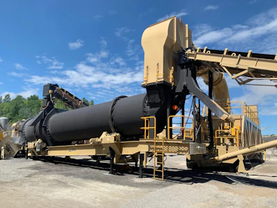 Large industrial rotary drum machine on gravel site with yellow equipment and blue sky