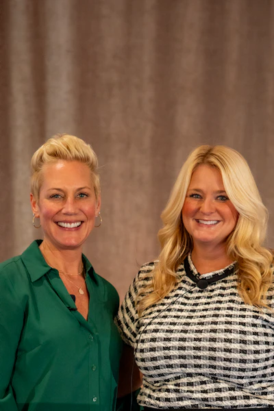 Two smiling blonde women in professional business attire standing together