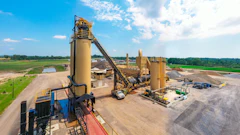 Industrial asphalt production facility with large yellow machinery under blue sky