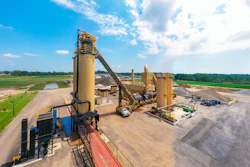 Industrial asphalt production facility with large yellow machinery under blue sky