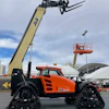 Orange JLG tracked telehandler with extended lifting arm at outdoor industrial event