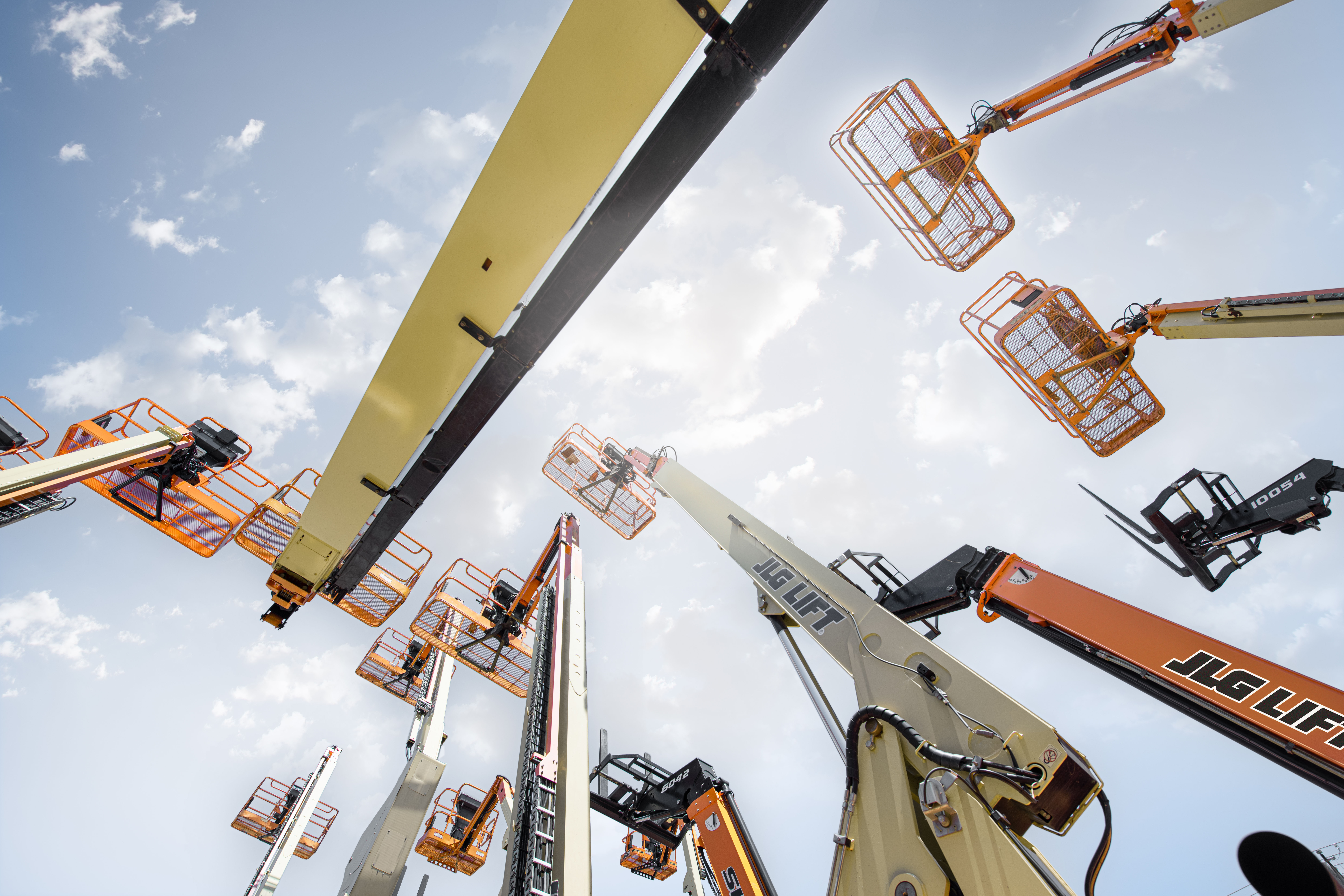Multiple aerial work platforms and boom lifts extended against blue sky