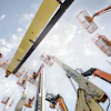 Multiple aerial work platforms and boom lifts extended against blue sky