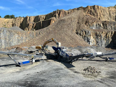 Stone quarry with excavator processing rock near steep rocky cliff face