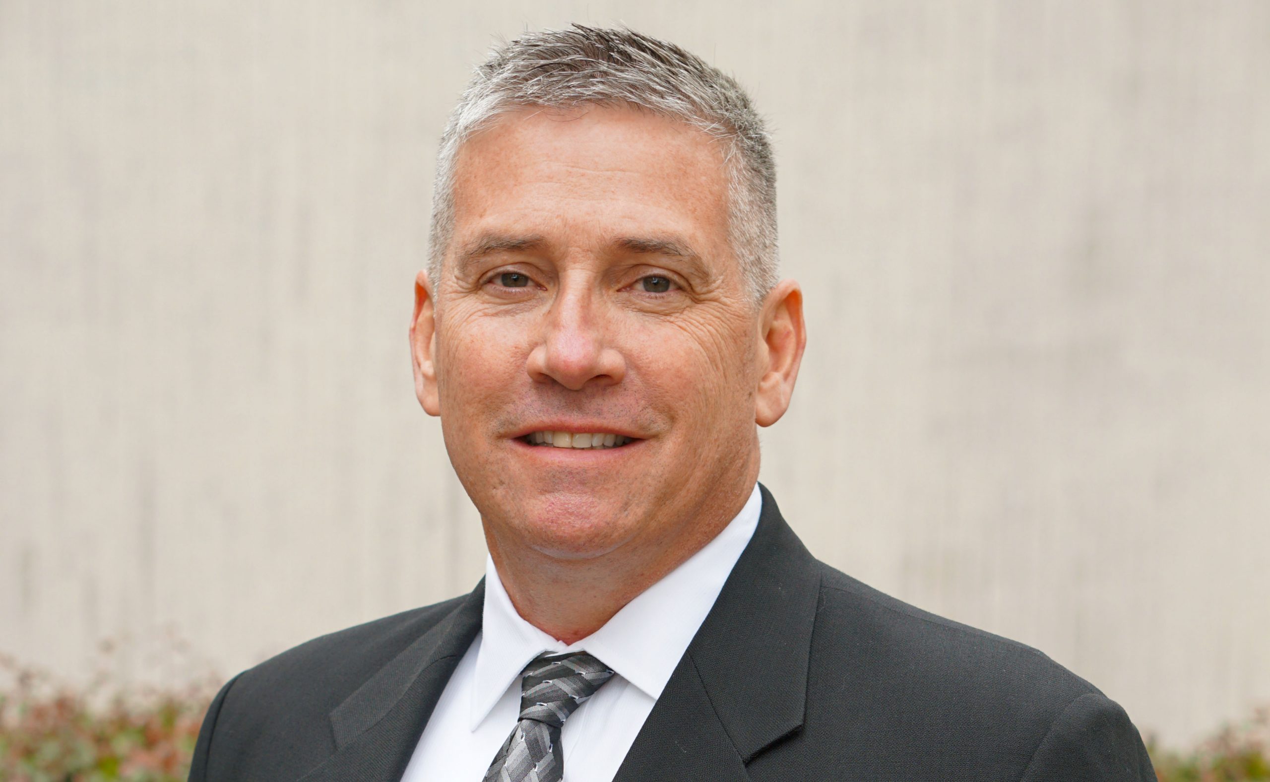 Professional businessman in gray suit and tie, smiling against neutral background