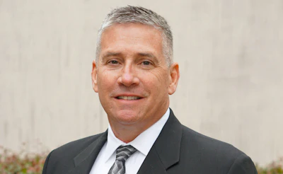 Professional businessman in gray suit and tie, smiling against neutral background