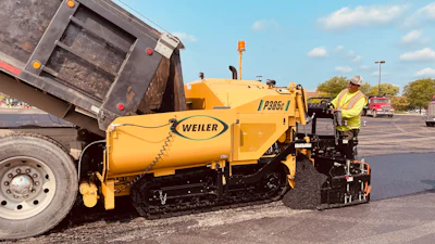 Yellow Weiler road paver laying asphalt with dump truck in industrial parking lot