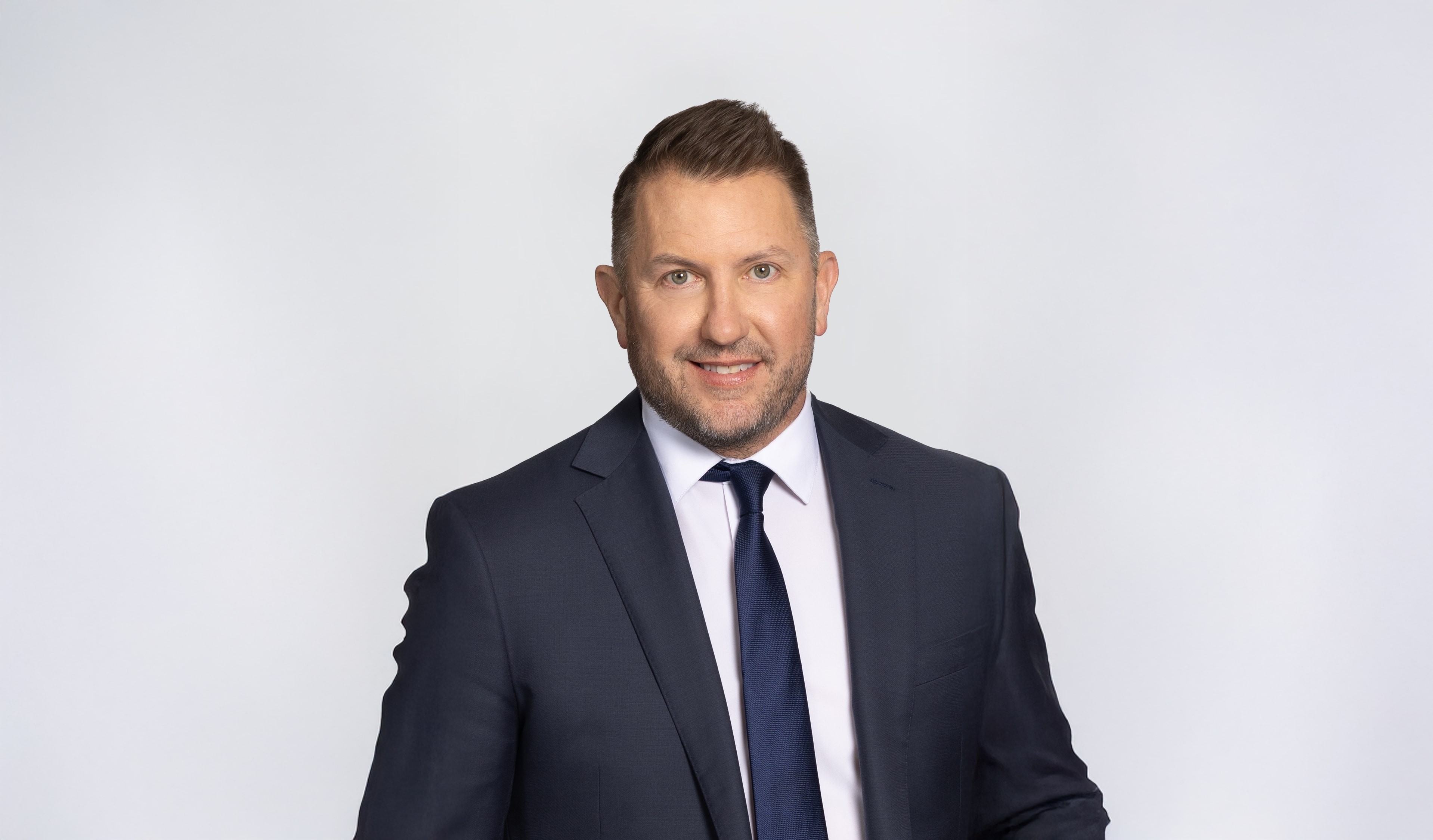 Professional businessman in navy suit and blue tie smiling against neutral background