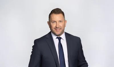 Professional businessman in navy suit and blue tie smiling against neutral background
