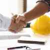 Construction professionals shaking hands over work documents with yellow hard hat