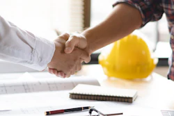 Construction professionals shaking hands over work documents with yellow hard hat