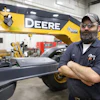 John Deere technician standing beside heavy construction equipment in workshop