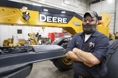 John Deere technician standing beside heavy construction equipment in workshop